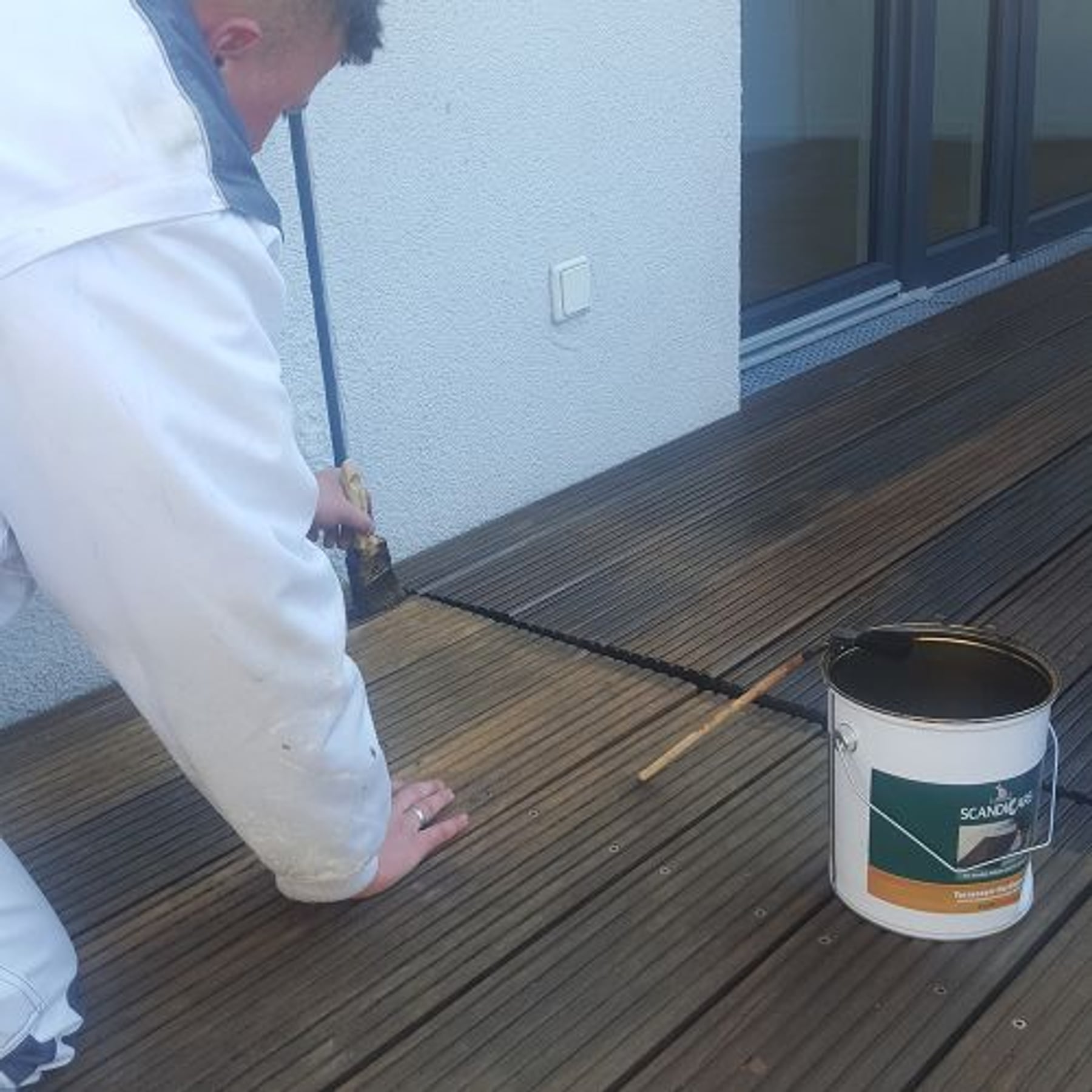 Lars Wilms behandelt eine Holzterrasse mit dem Pinsel